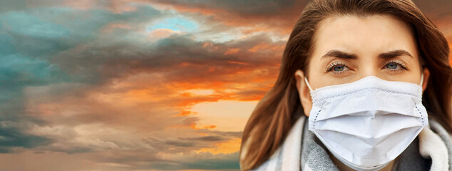 Wall Mural - health, safety and pandemic concept - close up of young woman wearing protective medical mask outdoors over sunset sky background