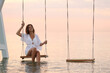 © New Africa - Young woman enjoying sunrise on swing over water