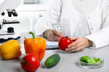 Wall Mural - scientist with fresh vegetables and clipboard at table in laboratory, closeup. poison detection