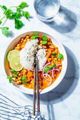 Wall Mural - Vegan chickpea curry with rice and cilantro in white bowl, white marble background. Indian cuisine concept.