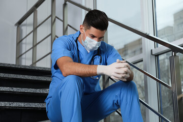 Poster - Sad doctor in facial mask on stairs indoors. Stress of health care workers during coronavirus pandemic