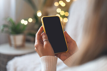 Cropped of woman's hands in white sweater holding mobile smart phone with blank screen of gadget at home. Digital mobile phone with copy space area.