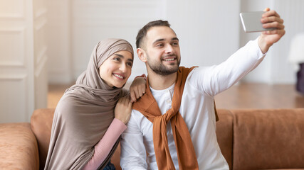 Wall Mural - Cheerful Muslim Spouses Making Selfie On Mobile Phone At Home