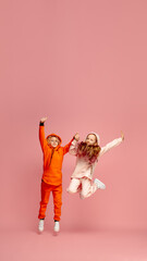 Wall Mural - Flyer. Happy children isolated on coral pink studio background. Look happy, cheerful. Copyspace for ad. Childhood, education, emotions, facial expression concept. Jumping high, playing, having fun.