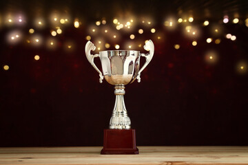 Wall Mural - image of gold trophy over wooden table and dark background, with abstract shiny lights