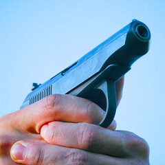 Wall Mural - Gun in the hands of a man against blue sky