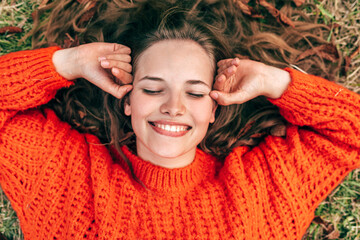 overhead candid portrait of a beautiful young woman wearing a knitted orange sweater lying on the gr