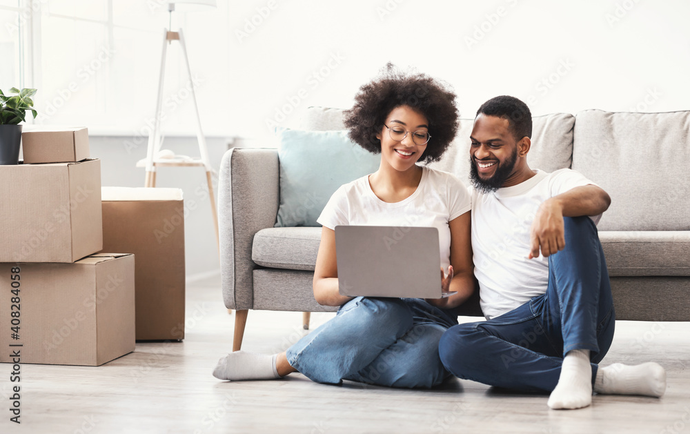 Black Couple Using Laptop Sitting Among Moving Boxes In House - obrazy, fototapety, plakaty 