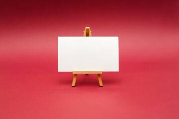 Wall Mural - White sheet on wooden easel, isolated on red background.