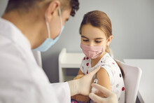 Brave Girl In Face Mask Looking At Needle In Doctor's Hands While Getting A Flu Shot At Clinic Or Hospital. Medical Worker Injecting Little Kid With Covid-19 Vaccine. Immunization For Children Concept