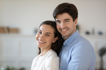 Wall Mural - Head shot portrait close up smiling man hugging attractive woman from back, young couple posing for family photo together, standing at home, happy wife and husband embracing, looking at camera