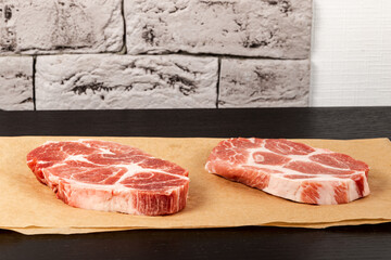 fresh raw marbled meat pork steak on brown parchment paper on black table against gray brick wall background