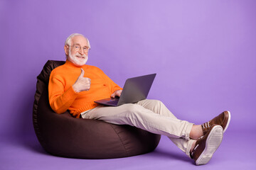 Sticker - Full body profile portrait of positive man sit soft chair show thumb up wear pants shoes isolated on purple color background