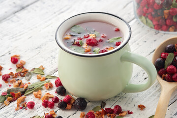Wall Mural - Cup of healthy fruit tea with apples, orange, red and black currant berries. Wooden spoon of dry ingredients for making tea.