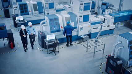 Fototapete - Industry Four Factory: Female Executive and Chief Engineer Inspect Facility Workshop, Look at robot arm working on Assembly Line. High-End CNC Machinery and Equipment. High Angle
