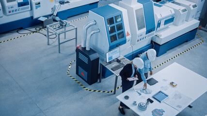 Fototapete - Industry Four Factory: Female Executive and Chief Engineer Inspect Facility Workshop, Look at robot arm working on Assembly Line, Analyze Blueprints High-End CNC Machinery and Equipment. High Angle