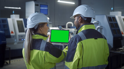 Wall Mural - Industry 4.0 Factory: Chief Engineer and Project Supervisor in Safety Vests and Hard Hats, Talk, Use Digital Tablet Computer with Green Screen, Chroma Key. Workshop with Machinery.