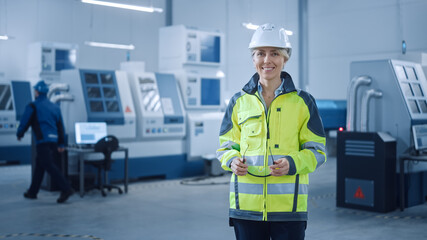 Poster - Beautiful Smiling Female Engineer Wearing Safety Vest and Hardhat Holds Safety Goggles. Professional Woman Working in the Modern Manufacturing Factory. Facility with CNC Machinery and robot arm