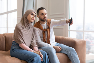 Wall Mural - Bored Muslim Couple Watching Television Switching Channels Sitting At Home