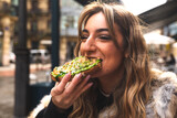 Fototapeta Uliczki - Young caucasian woman having breakfast at a terrace eating an avocado toast.
