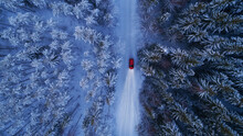 Winter Landscape With Red Car Driving At Night. Lights Of Car And Winter Snowy Road In Dark Forest, Big Fir Trees Covered Snow. Top Down View. 