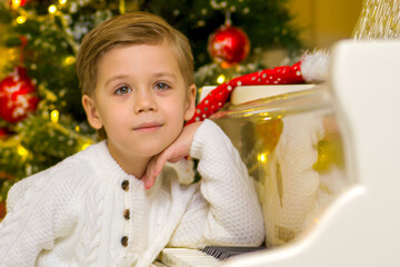 Wall Mural - A little boy is sitting at the piano near the Christmas tree.