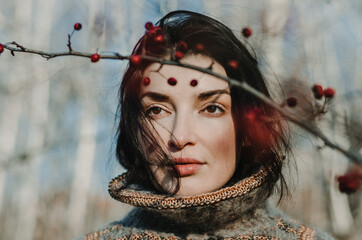 Wall Mural - Front view close up portrait of a brunette caucasian woman with a queen neck sweater, framed by a branch of winter berries, in a forest