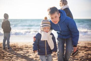 Happy family, mother with sons walking wirh fun in the sea shore on windy day. People dressed warm clothes.