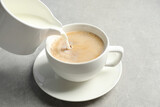 Fototapeta Mapy - Pouring milk into cup of hot coffee on grey table