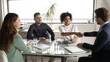 © fizkes - Happy diverse business partners shaking hands at meeting in modern boardroom, group negotiations, African American businesswoman and businessman making agreement, great deal, signing contract