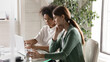 © fizkes - Confident African American mentor teaching new employee, using laptop, pointing on laptop screen, helping with corporate software, diverse colleagues working on project, sharing ideas, talking