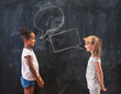 Two little girls having a debate in front of blackboard in classroom at school