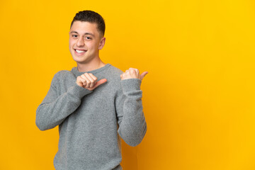 Wall Mural - Young caucasian man isolated on yellow background pointing to the side to present a product