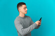 © luismolinero - Young caucasian man isolated on blue background sending a message or email with the mobile
