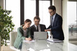 © fizkes - Three colleagues with team leader wearing glasses working on project together, sitting at office desk with laptop, discussing strategy, sharing business ideas, brainstorming, mentor training staff