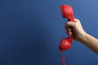 Closeup view of woman holding red corded telephone handset on blue background, space for text. Hotline concept