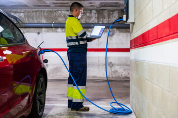 Professional male technician programming on laptop while charging electric car