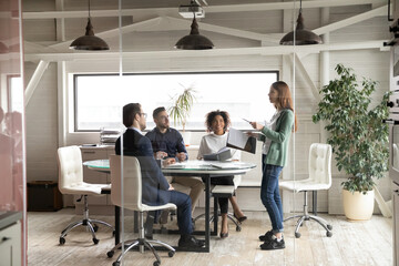 Wall Mural - Diverse colleagues listening to businesswoman leader at meeting in boardroom view behind glass wall, confident mentor training staff, leading briefing, business partners group negotiations