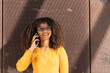 © NOVELLIMAGE/Westend61 - Smiling young woman talking on mobile phone against wall on sunny day