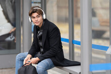 Handsome Man Listening Music Looking Away While Sitting At Bus Stop