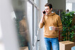 © Giorgio Fochesato/Westend61 - Smiling man talking on phone call while holding coffee cup by window in new home