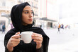 © Jose Carlos Ichiro/Westend61 - Portrait of young beautiful woman wearing black¬†hijab¬†enjoying cup of coffee at sidewalk cafe
