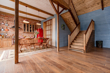 cozy all wooden interior of a country house in a wooden design. spacious living room with kitchen area with large windows. bedroom on the second floor.