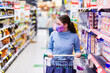 © Clare Seibel-Barnes/Austockphoto - Young woman in her twenties wearing a face mask in shopping aisle, choosing what to buy