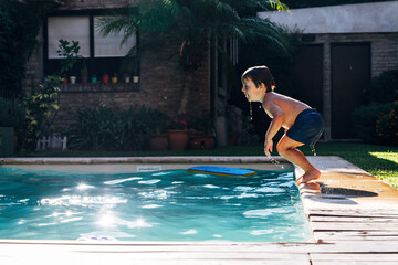 Little boy jumping in a pool. Child get fun in the swimming pool of his home. Outdoors activities in quarantine.