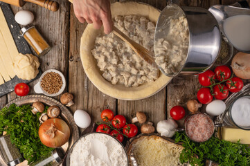 The chef prepares and works with the dough making a pie with mushrooms and meat. Cooking ingredients tomatoes, onions, mushrooms and meat. Top view. Cooking cooking concept and recipe book.