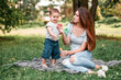 © zadorozhna - Mother with son blowing soap bubbles in the park.