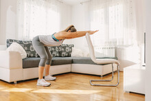 Muscular Sportswoman In Shape Doing Fitness Exercises For Her Backs While Leaning On Chair. If You Can't Go To The Gym, You Can Make Your Own At Home.