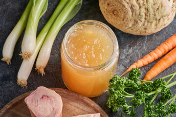 Cooled congealed beef bone broth in a glass jar, with vegetables and marrow bones in the background