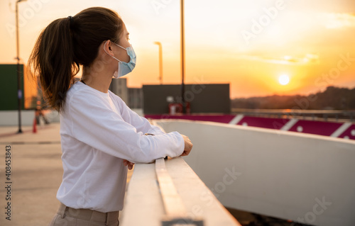 Side view of loneliness woman wearing mask and looking to beautiful sunset. She hope everything will be better.
